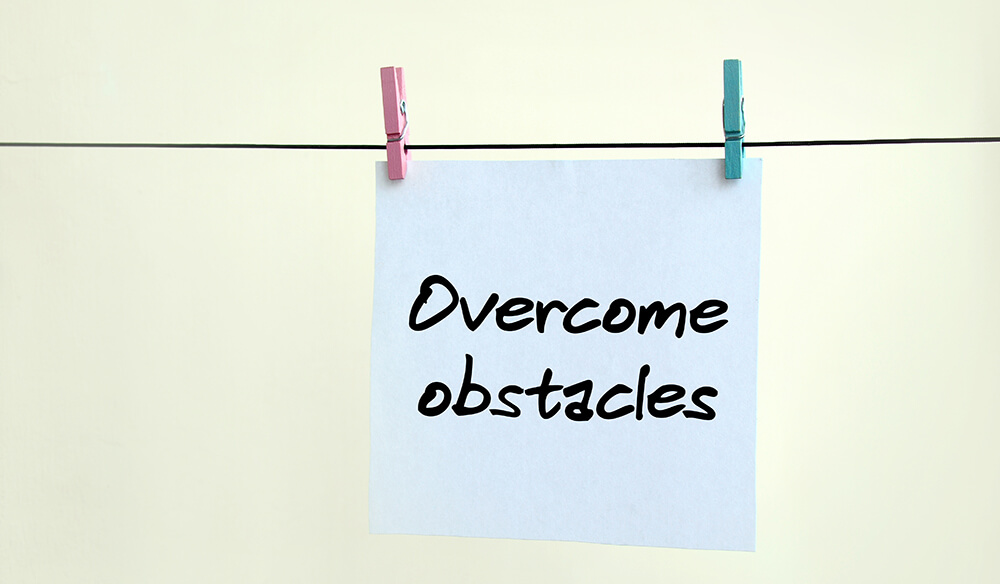 Overcome obstacles. Note is written on a white sticker that hangs with a clothespin on a rope on a background of beige wall
